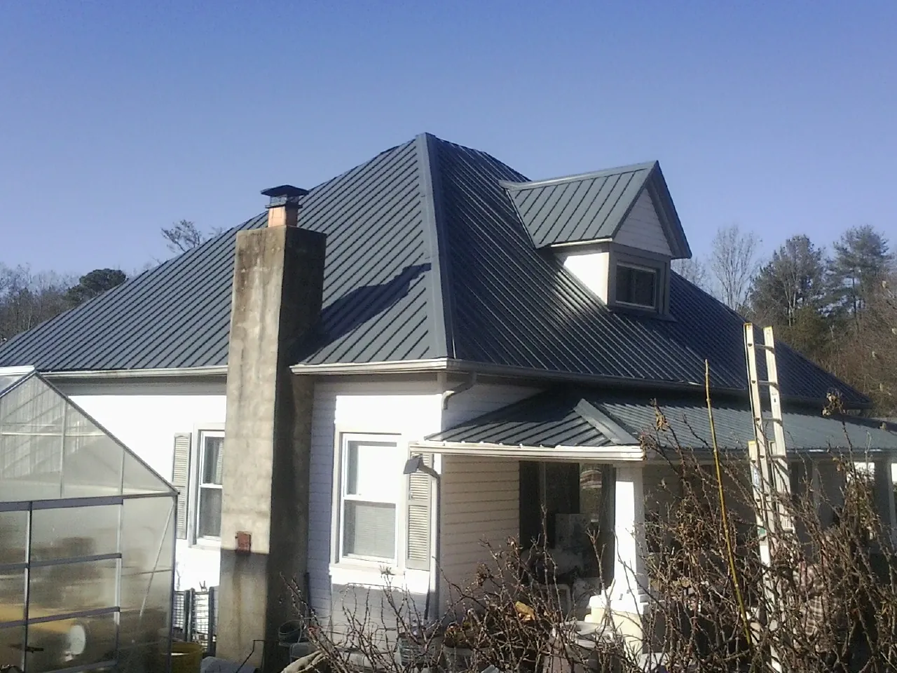 Dark blue standing seam metal roof on a white farmhouse with dormer — Slate & Tile Roof Repair by Roofing Brothers in Sundance