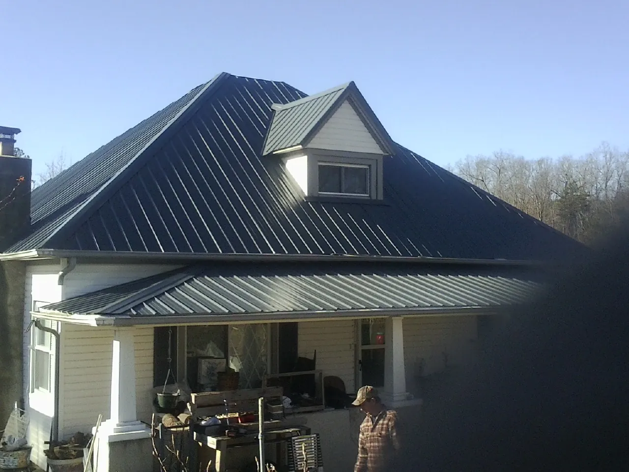 Dark blue standing seam metal roof with a dormer above a front porch in Sundance