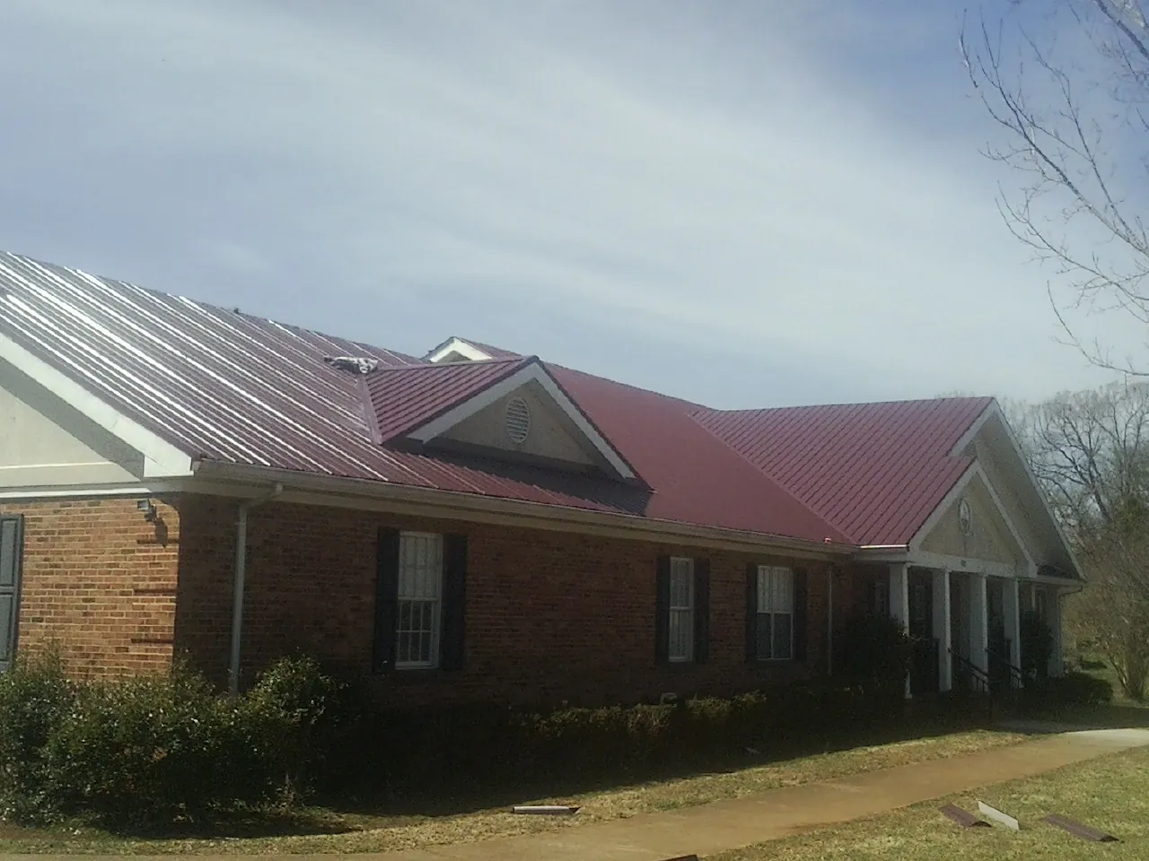 Red metal roof with gabled entries on a long brick building, from a Hail Damage Roof Repair job in Sundance