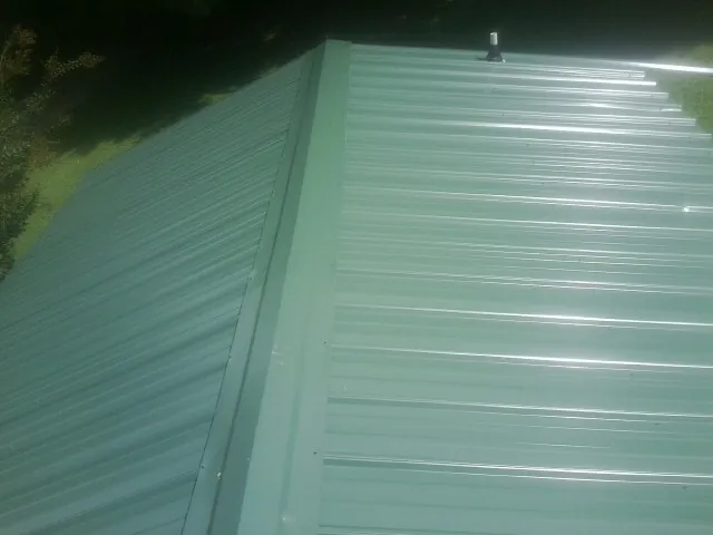 New green metal panels meeting at the ridge of a roof — Flat Roof Repair work by our crew in Sundance