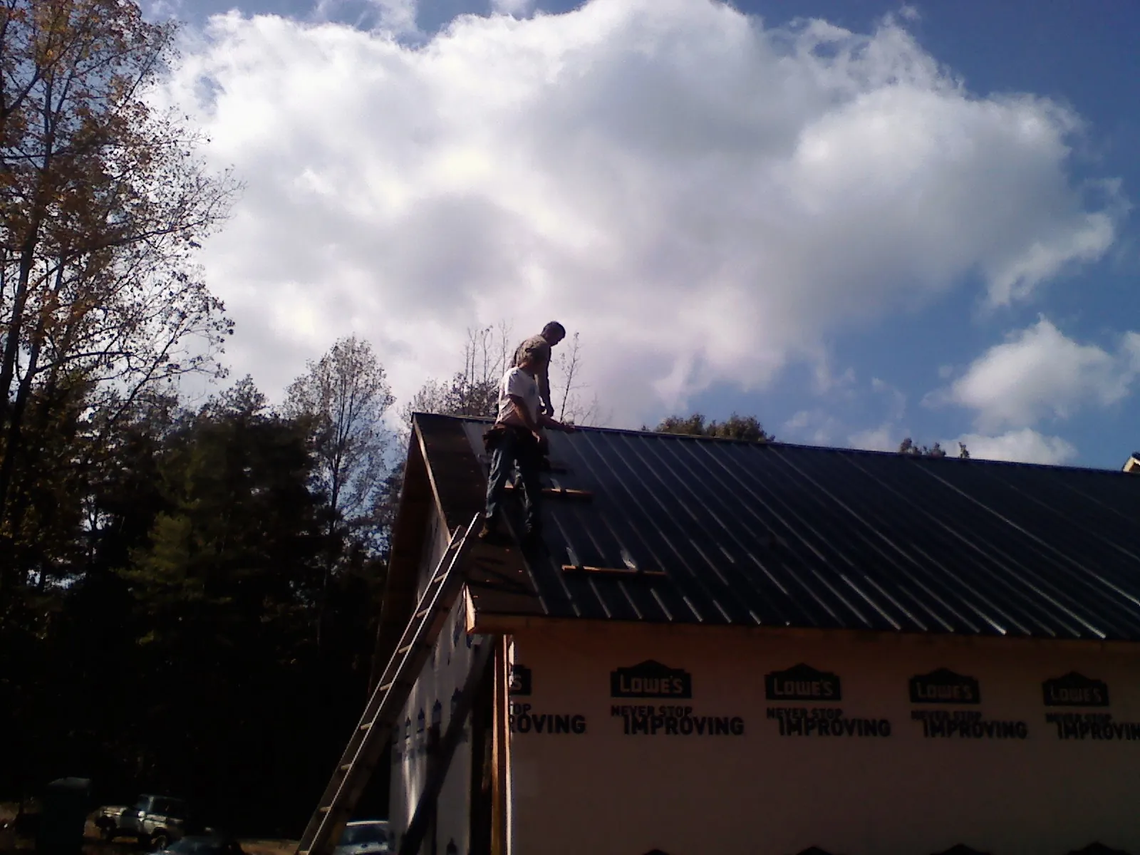 Roofer fastening dark metal panels high against a cloudy sky, from a Roof Inspection job in Sundance