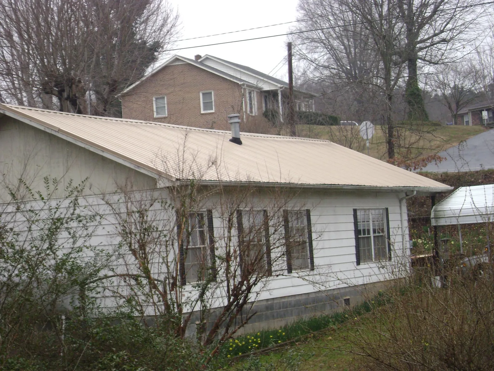 Tan metal roof on a white sided house set into a hillside — Commercial Roofing by Roofing Brothers in Sundance