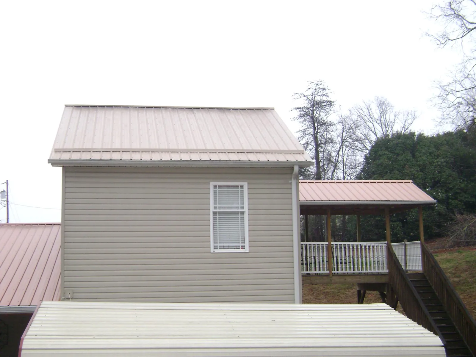 Tan metal roofs on a two story addition and attached porch, from a Roof Replacement job in Sundance